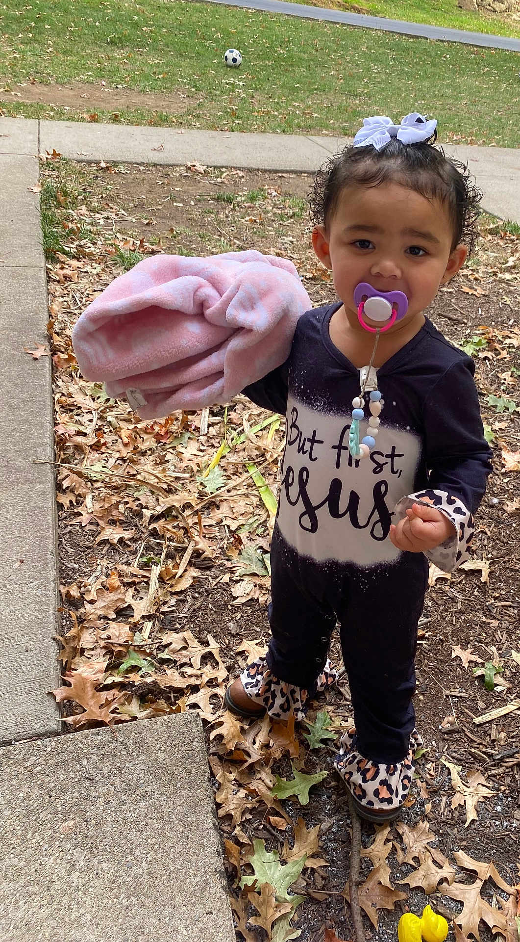Nevayla is registered to the contest to win money with this photo: toddler, child, pacifier, blanket, outdoor, grass, leaves, sidewalk, curly_hair, bow, boots, black_clothing, patterned_clothing, fall, nature, young_child, person, standing, cute, curious