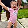 Chloe is registered to the contest to win money with this photo: adult_hand, baby, child, clothing, daylight, family, grass, happy, nature, outdoor, person, pink_onesie, playful, shoes, shorts, sidewalk, smiling, support, toddler, walking