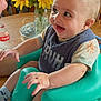 Karson is registered to the contest to win money with this photo: baby, smiling, baby_seat, indoor, sunflowers, table, person, face, happy, clothing, bottle, wooden_furniture, hand, socks, blue, green, yellow, flower, expression, closeup