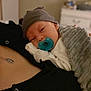 Damian joined the competition — help win amazing prizes! baby, pacifier, hat, blanket, person, indoor, resting, sleepy, comfort, closeup, skin, clothing, necklace, black_shirt, bedroom, furniture, soft_texture, warm, infant, human