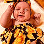 arm, baby, blanket, cheeks, child, closeup, clothing, cute, face, fist, happy, headband, infant, lying_down, portrait, skin, smile, soft_texture, sunflower_pattern, winking