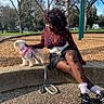 Boo is registered to the contest to win money with this photo: affection, black_shoes, casual, concrete_wall, curly_hair, daytime, dog, fashion, fishnet_stockings, grass, leash, outdoor, park, person, pink_harness, sitting, smiling, sunny, trees, wood_chips