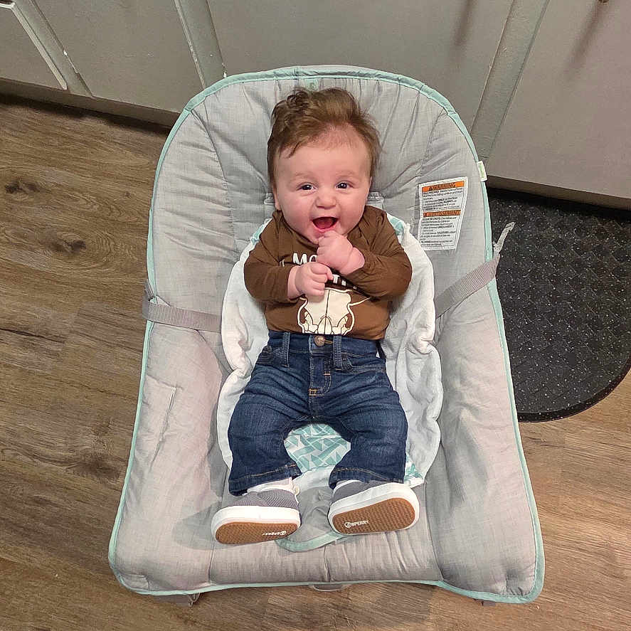 Adam joined the competition — help win amazing prizes! baby, child, infant, smiling, happy, seated, bouncer, baby_chair, indoor, kitchen, cabinets, wood_floor, adult_feet, clothing, brown_shirt, jeans, shoes, portrait, home, photography