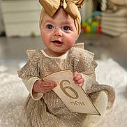 Anaya participe au concours pour gagner de l'argent avec cette photo : baby, blue_eyes, bow, child, cozy, cute, dress, face, floor, hands, headband, home, indoor, infant, milestone_card, portrait, rug, sitting, smiling, soft_texture