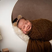 Bear is registered to the contest to win money with this photo: baby, sleeping, newborn, brown_blanket, headband, crescent_moon, fluffy_cushion, polka_dot_lamp, wooden_block, cozy, soft_texture, portrait, indoors, warm_colors, cute, peaceful, wrapped, infant, props, photography