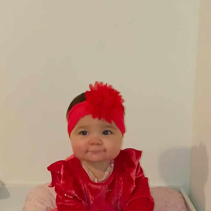 Alyzée a rejoint le concours — aidez-le/la à gagner de superbes lots ! adorable, baby, baby_bedding, child, comfort, cute, flower, happy, headband, heart_pattern, indoors, infant, pink_cushion, portrait, red_dress, sitting, smiling, soft_lighting, white_tights, young_child