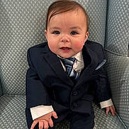 Ares joined the competition — help win amazing prizes! baby, child, suit, tie, armchair, smile, cute, formal_clothing, person, indoor, portrait, young_child, fashion, seated, hands, face, hair, buttoned_jacket, patterned_fabric, candid