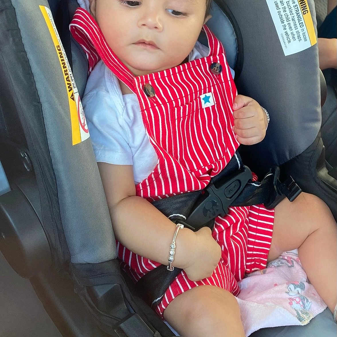 Jahnaav is registered to the contest to win money with this photo: ankle_bracelet, baby, bracelet, car, car_seat, child, clothing, cute, foot, hand, indoors, infant, person, portrait, red_overalls, safety_belt, seat, seat_belt, white_shirt, young_child
