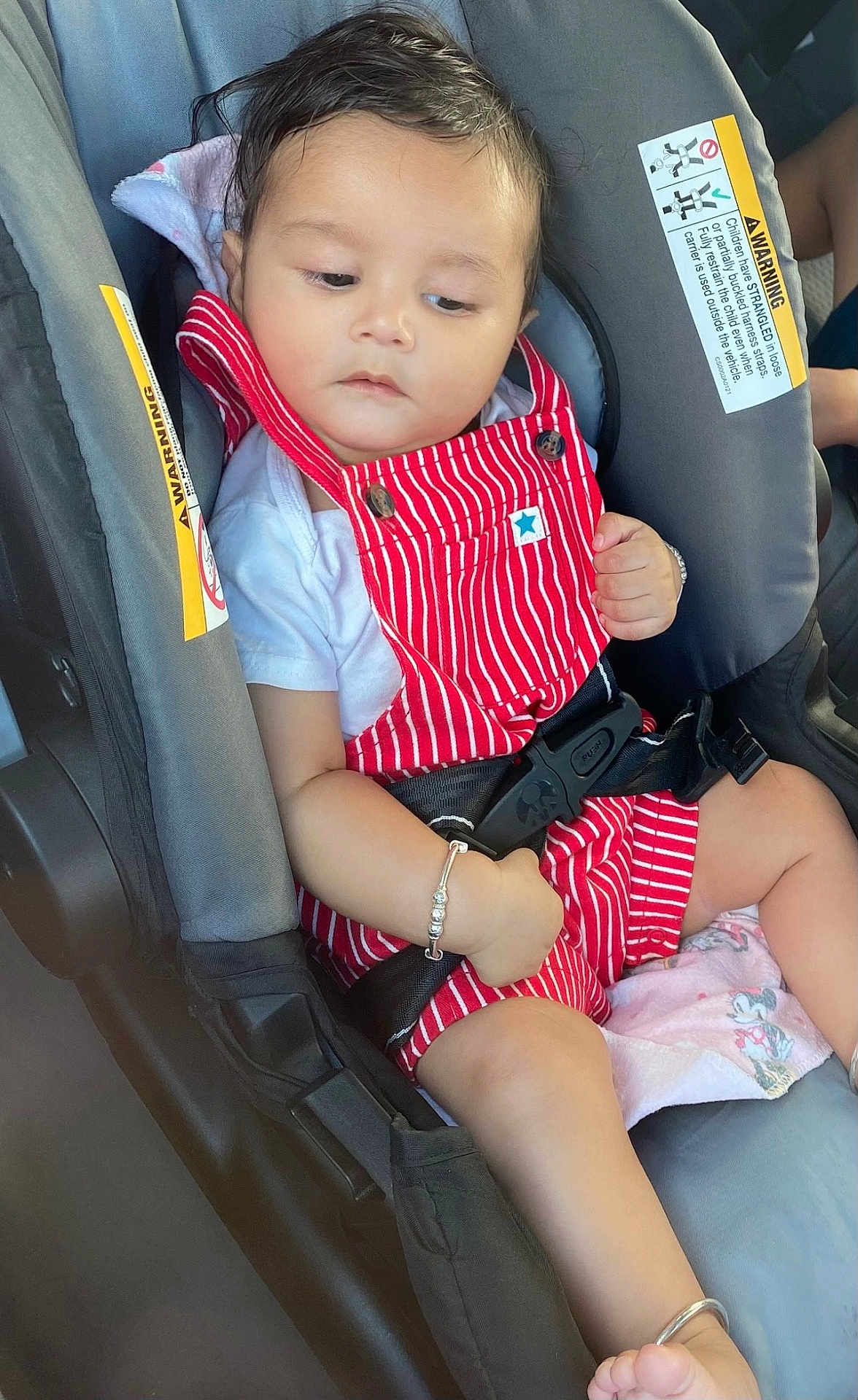Jahnaav is registered to the contest to win money with this photo: baby, child, car_seat, red_overalls, white_shirt, bracelet, ankle_bracelet, safety_belt, seat_belt, car, infant, cute, portrait, indoors, seat, young_child, person, clothing, hand, foot