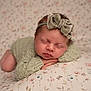newborn, baby, sleeping, headband, bow, knitted_clothing, blanket, floral_pattern, soft_texture, portrait, peaceful, infant, cute, resting, closeup, child, indoors, cozy, warm, tender
