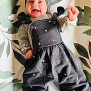Ottilie is registered to the contest to win money with this photo: baby, smiling, headband, gray_outfit, hearts, striped_shirt, hand, face, happy, lying_down, leaf_pattern, background, cute, infant, clothing, waving, child, portrait, indoor, young
