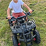 child, boy, smiling, atv, toy_vehicle, outdoor, grass, play, summer, casual, happy, handlebars, shorts, white_shirt, young, fun, leisure, vehicle, childhood, nature