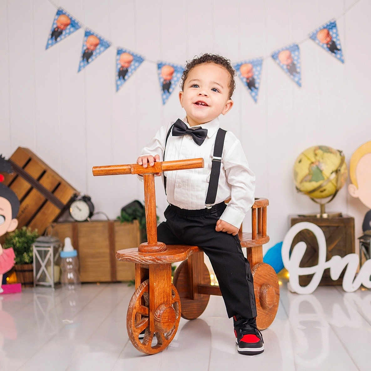 Theon joined the competition — help win amazing prizes! banner, birthday, black_pants, bow_tie, cartoon_cutouts, celebration, child, floor_reflection, gift_box, globe, indoors, lantern, party_decorations, smiling, sneakers, suspenders, toddler, toy, white_shirt, wooden_tricycle