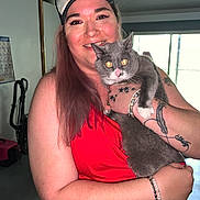 Martini Coons is registered to the contest to win money with this photo: bracelet, cap, cat, face, gray_cat, happy, holding, home_interior, indoor, long_hair, natural_light, person, pet, portrait, red_top, smiling, tattoo, vacuum_cleaner, white_paws, window