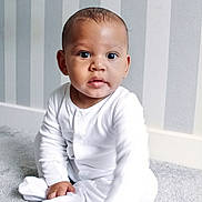 Kyrie is registered to the contest to win money with this photo: baby, child, infant, pajamas, white_clothing, carpet, floor, indoor, portrait, curious, reaching_hand, striped_wallpaper, home, cute, young_child, sitting, soft_lighting, person, expression, cozy