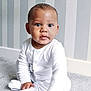 baby, child, infant, pajamas, white_clothing, carpet, floor, indoor, portrait, curious, reaching_hand, striped_wallpaper, home, cute, young_child, sitting, soft_lighting, person, expression, cozy