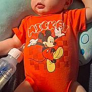 Levi joined the competition — help win amazing prizes! baby, infant, onesie, mickey_mouse, orange_clothing, bottle, cushion, soft_toy, lying_down, child, cute, portrait, indoors, skin, face, head, hand, leg, comfortable, expression