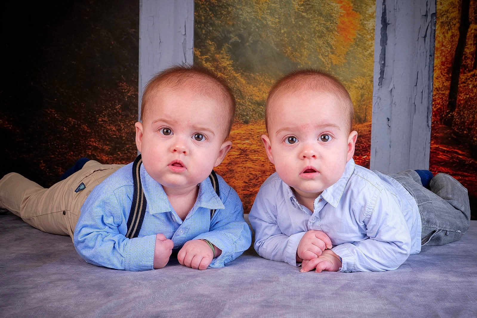 Côme Et Marceau a rejoint le concours — aidez-le/la à gagner de superbes lots ! baby, twin_babies, infant, portrait, studio, lying_down, blue_shirts, suspenders, pants, siblings, curious_expression, wide_eyes, hands, blanket, floor, backdrop, autumn_background, wood_pillars, photography, cute