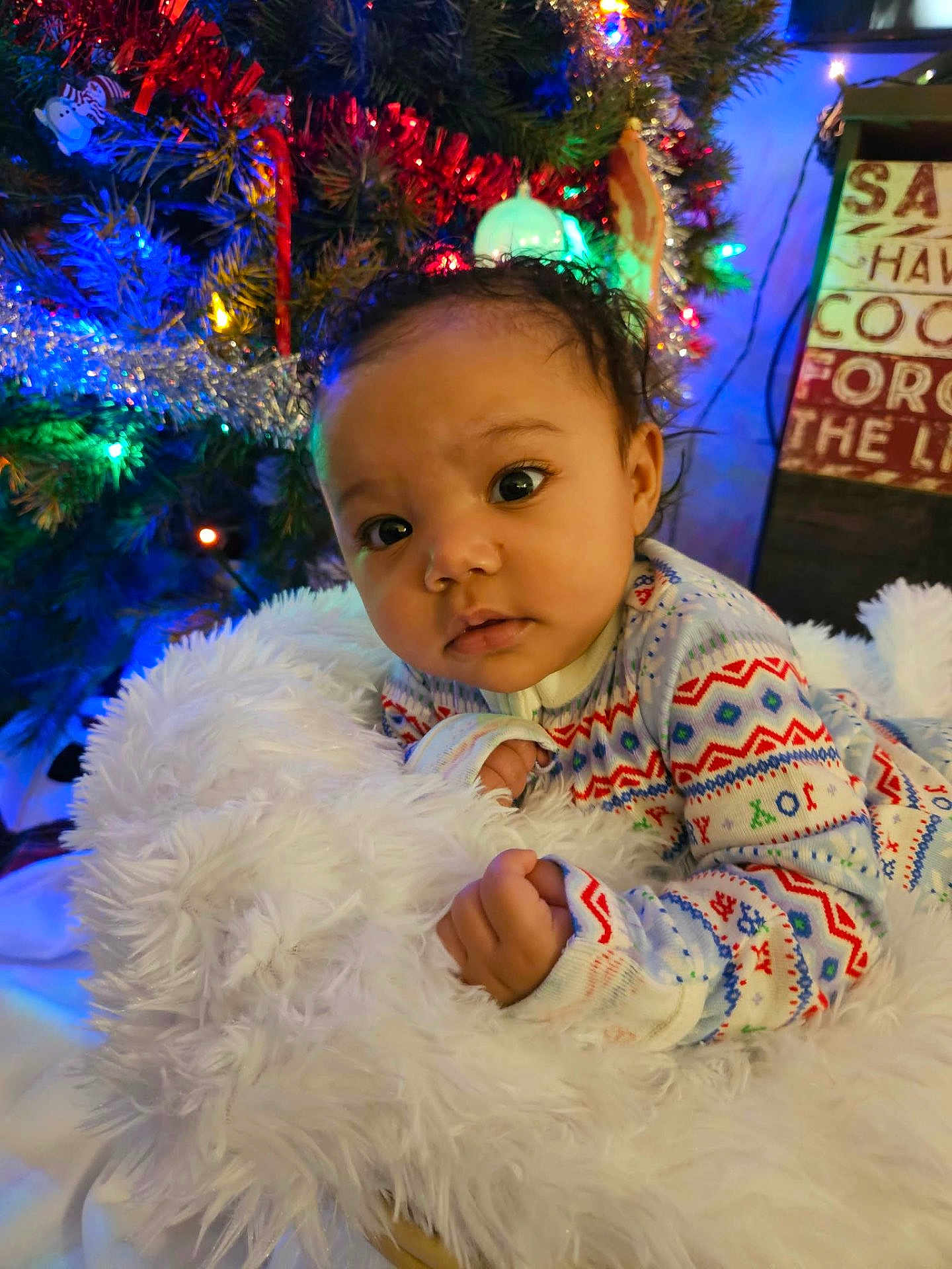 Serinity is registered to the contest to win money with this photo: baby, infant, child, onesie, blanket, fluffy, christmas_tree, holiday_lights, decorations, festive, face, curious, indoors, cozy, portrait, soft_lighting, cute, holiday, warm, colorful