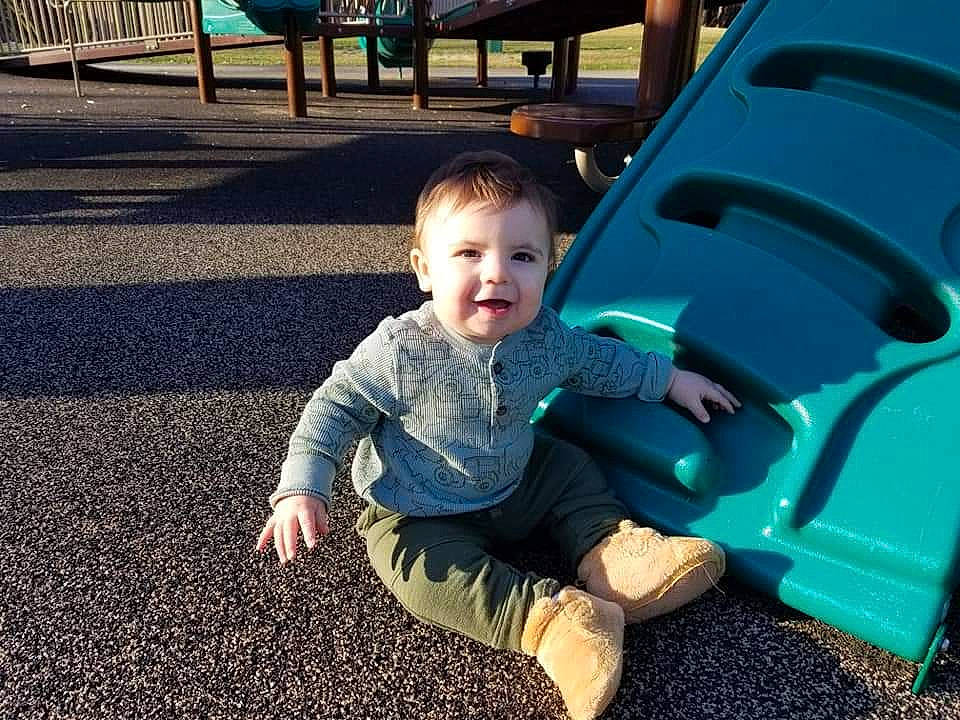 Anderson is registered to the contest to win money with this photo: baby, baby_toddler_clothing, child, chute, city, facial_expression, flooring, fun, grass, happy, human_body, leisure, people_in_nature, person, play, playground, public_space, recreation, sitting, smile