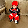 baby, beige_couch, black_shirt, bow_tie, carpet, child, clothing, couch, cute, happy, holiday_outfit, indoors, infant, looking_at_camera, portrait, red_hat, red_pants, sitting, valentine, wall