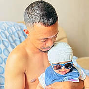 Censio is registered to the contest to win money with this photo: man, baby, child, hat, sunglasses, shirtless, indoor, couch, blanket, holding, person, family, smile, cute, portrait, baby_clothes, hand, love, care, relax