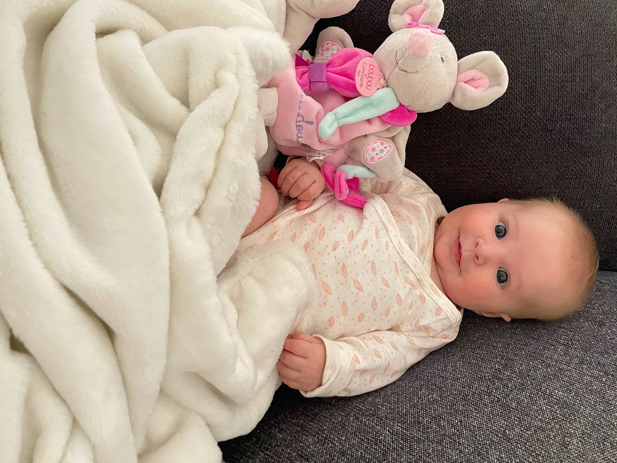 Ava a rejoint le concours — aidez-le/la à gagner de superbes lots ! baby, baby_products, baby_sleeping, baby_toddler_clothing, cheek, child, comfort, finger, gesture, happy, headgear, human_body, linens, nail, person, petal, pink, sitting, stuffed_toy, toddler