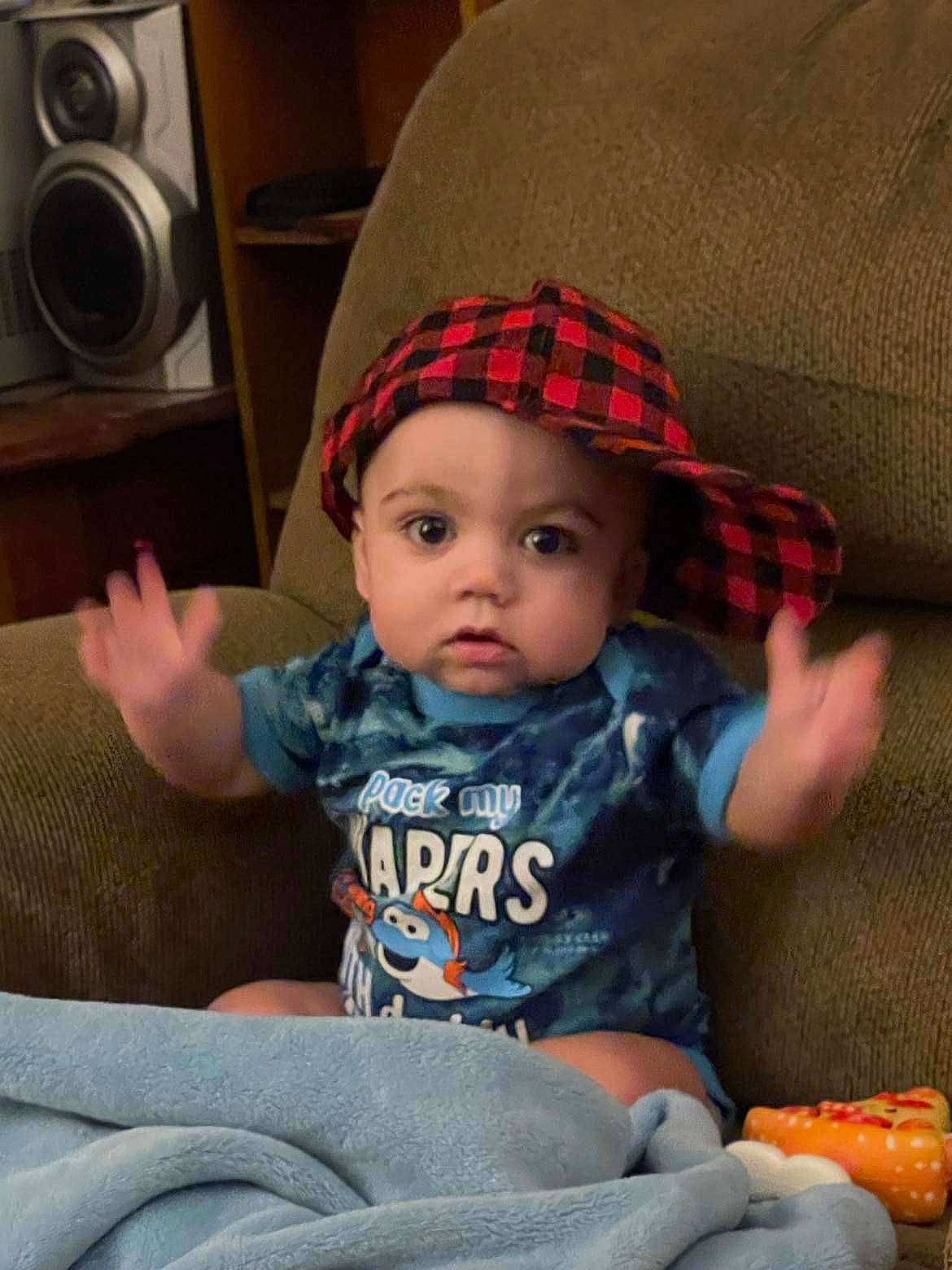 Johnathan is registered to the contest to win money with this photo: arm, baby, baby_toddler_clothing, cap, cheek, child, comfort, headwear, human_body, iris, lap, mouth, organ, person, plaid, product, sitting, skin, sleeve, t_shirt