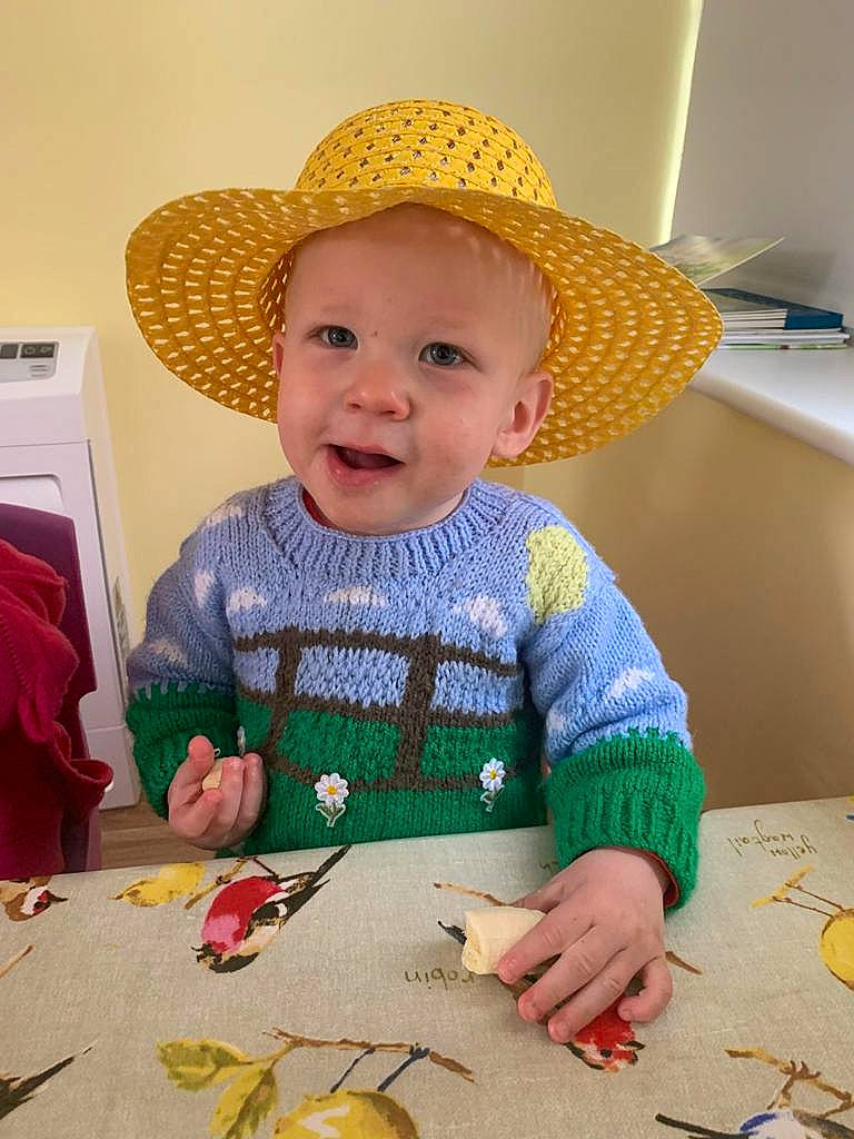 Oscar is registered to the contest to win money with this photo: art, baby, baby_toddler_clothing, chair, child, dress, fashion_accessory, fun, happy, hat, headgear, headwear, pattern, person, room, sitting, smile, sun_hat, table, tableware