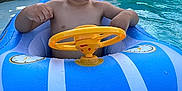 Aron is registered to the contest to win money with this photo: child, pool, inflatable, float, water, summer, outdoor, toy, blue, yellow, steering_wheel, swimming_pool, relaxing, sunny, vacation, young, boy, fun, play, backyard
