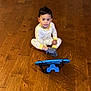 toddler, child, pajamas, banana_pattern, wooden_floor, toy_car, toy_dinosaur, toy_truck, tablet, indoor, playtime, colorful, sitting, floor, young_child, casual, home, electronics, curious, cute