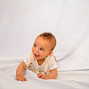 Ruben joined the competition — help win amazing prizes! baby, infant, child, smiling, happy, lying_down, white_background, overalls, curly_hair, cute, portrait, one_person, indoors, soft_lighting, toddler, skin, face, hands, white_clothing, expression