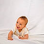 baby, infant, child, smiling, happy, lying_down, white_background, overalls, curly_hair, cute, portrait, one_person, indoors, soft_lighting, toddler, skin, face, hands, white_clothing, expression