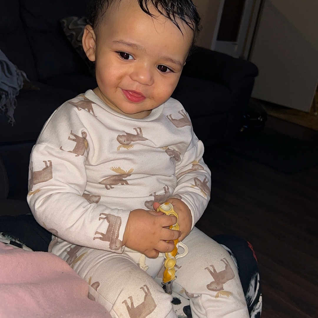 Kysonn is registered to the contest to win money with this photo: accessories, architecture, baby, bodypart, clothing, couch, face, finger, furniture, hand, happy, head, homedecor, pajamas, pants, person, photography, portrait, sitting, smile