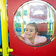 Hazel joined the competition — help win amazing prizes! child, playground, bubble_window, smile, happy, plastic, red_panel, yellow_pole, outdoor, play, fun, young_child, face, hand, casual_clothing, daylight, recreation, park, curious, cute