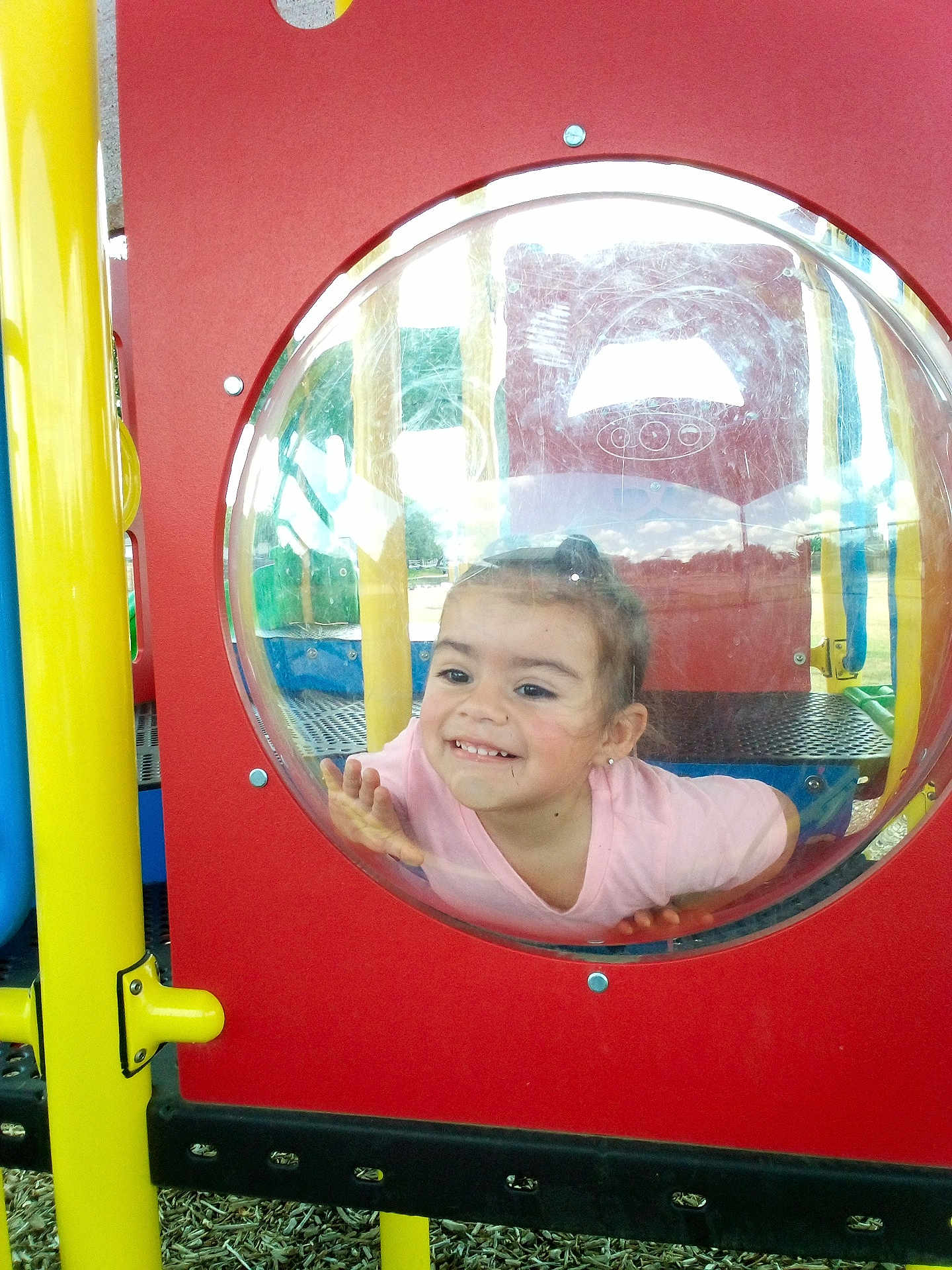 Hazel joined the competition — help win amazing prizes! child, playground, bubble_window, smile, happy, plastic, red_panel, yellow_pole, outdoor, play, fun, young_child, face, hand, casual_clothing, daylight, recreation, park, curious, cute