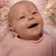 Rory is registered to the contest to win money with this photo: baby, infant, newborn, smiling, portrait, face, eyes, mouth, ear, pink_sweater, knitwear, floral_background, bokeh, close_up, skin, cheek, head, happy, lying_down, studio_photography