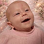 baby, infant, newborn, smiling, portrait, face, eyes, mouth, ear, pink_sweater, knitwear, floral_background, bokeh, close_up, skin, cheek, head, happy, lying_down, studio_photography