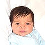 Salim is registered to the contest to win money with this photo: baby, infant, child, face, portrait, dark_hair, blue_clothing, looking_at_camera, serious_expression, indoors, light_background, closeup, cute, newborn, skin, young_child, person, baby_clothes, sitting, head