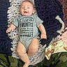 Waylon joined the competition — help win amazing prizes! baby, infant, onesie, text_on_clothing, blanket, knitted_blanket, happy, smiling, lying_down, footwear, football_pattern, clothing, camouflage, pants, person, indoors, cozy, cute, newborn, relaxed