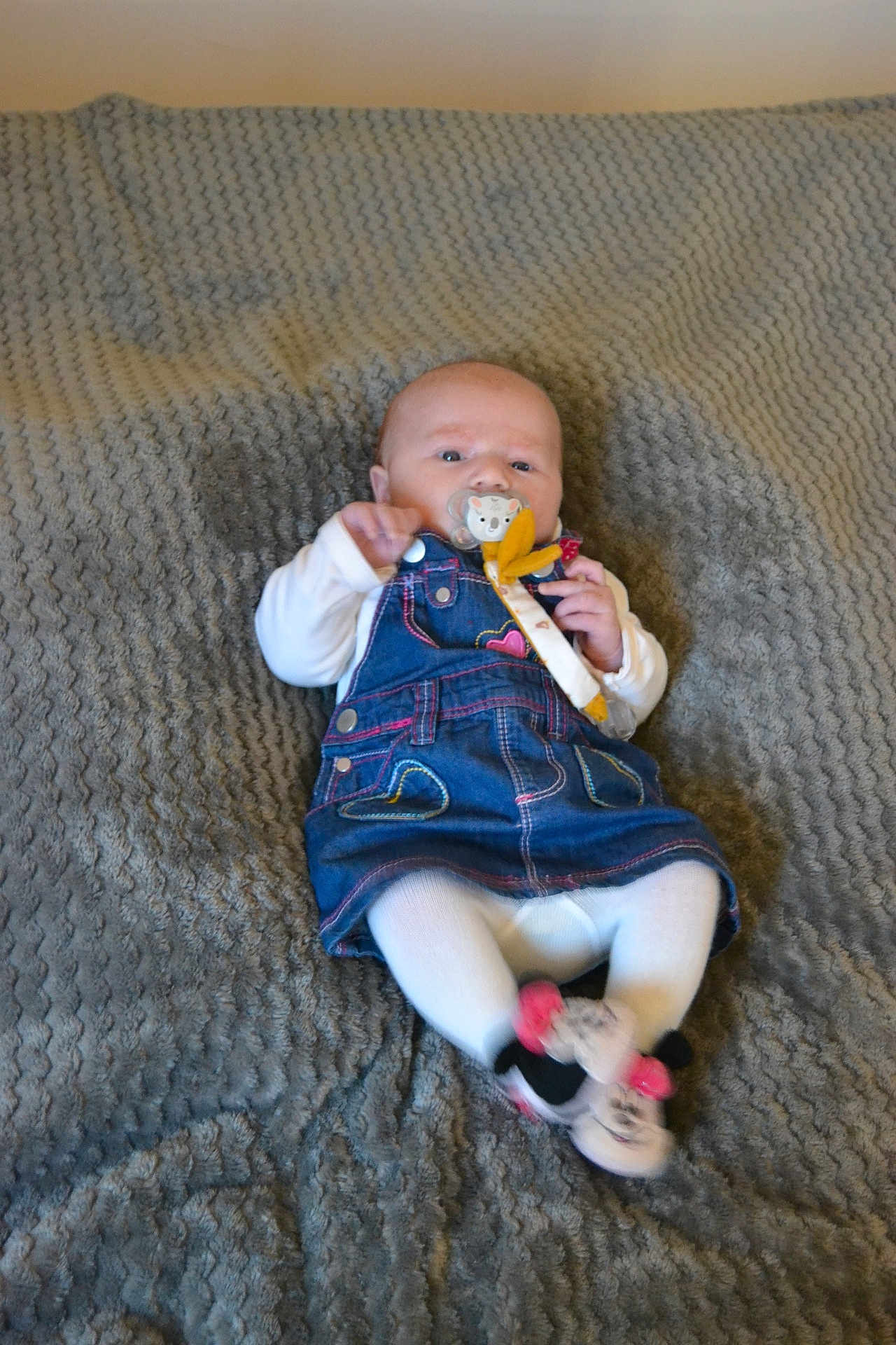 Iris participe au concours pour gagner de l'argent avec cette photo : baby, infant, pacifier, denim_dress, white_tights, slippers, minnie_mouse, blanket, textured, cute, child, lying_down, indoors, clothing, person, small, face, head, hands, feet