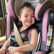 Natalia is registered to the contest to win money with this photo: child, toddler, car_seat, seatbelt, vehicle_interior, smiling, happy, safety, pink, gray, clothing, hair, skin, face, seat, window, daylight, armrest, hands, legs
