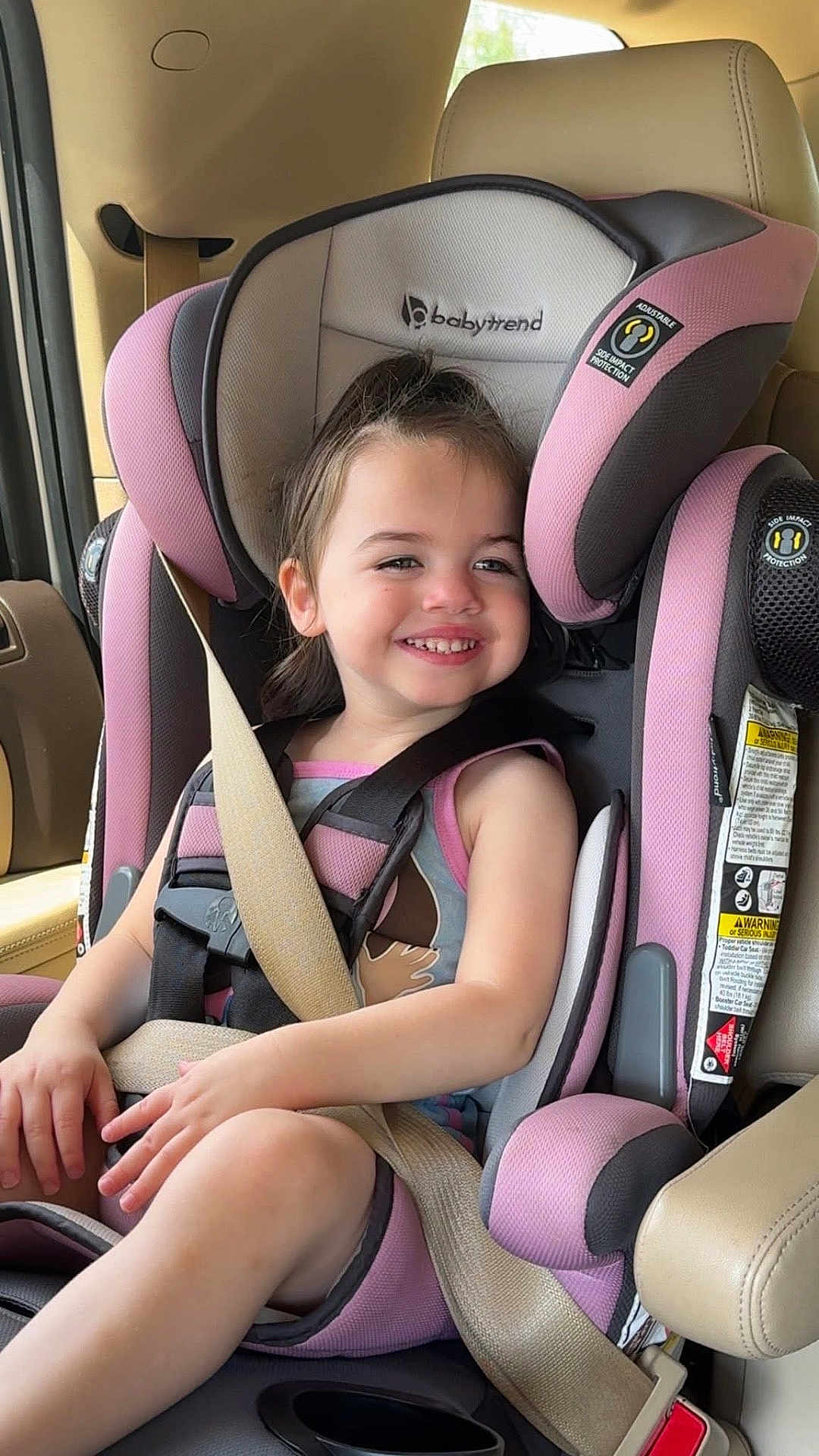 Natalia is registered to the contest to win money with this photo: child, toddler, car_seat, seatbelt, vehicle_interior, smiling, happy, safety, pink, gray, clothing, hair, skin, face, seat, window, daylight, armrest, hands, legs