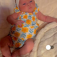 Kashlynn is registered to the contest to win money with this photo: baby, infant, blanket, headband, flower_pattern, clothing, blue_eyes, skin, cute, newborn, lying_down, soft_texture, hand, foot, yellow, white, portrait, child, sleepwear, fabric