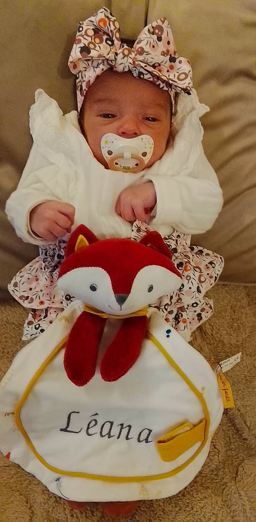 Léana a rejoint le concours — aidez-le/la à gagner de superbes lots ! baby, blanket, bow, carpet, child, cozy, cute, fox, headband, indoors, infant, name_tag, pacifier, patterned_skirt, plush_toy, portrait, sitting, soft_toy, white_clothing, young_baby
