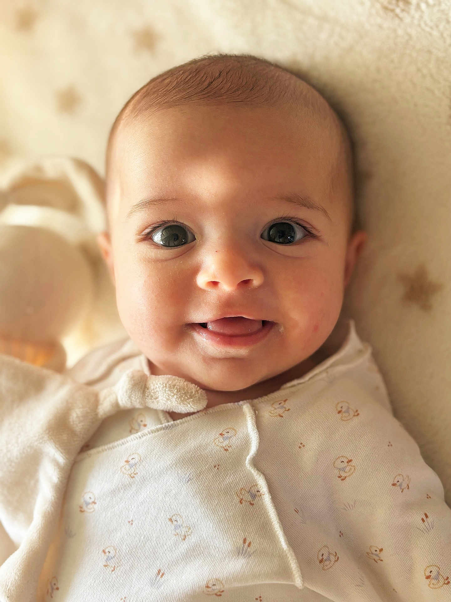 Maylee participe au concours pour gagner de l'argent avec cette photo : baby, infant, child, face, eyes, tongue, onesie, duck_print, blanket, star_pattern, soft_texture, closeup, portrait, cute, smile, skin, warm_light, cozy, lying_down, indoors