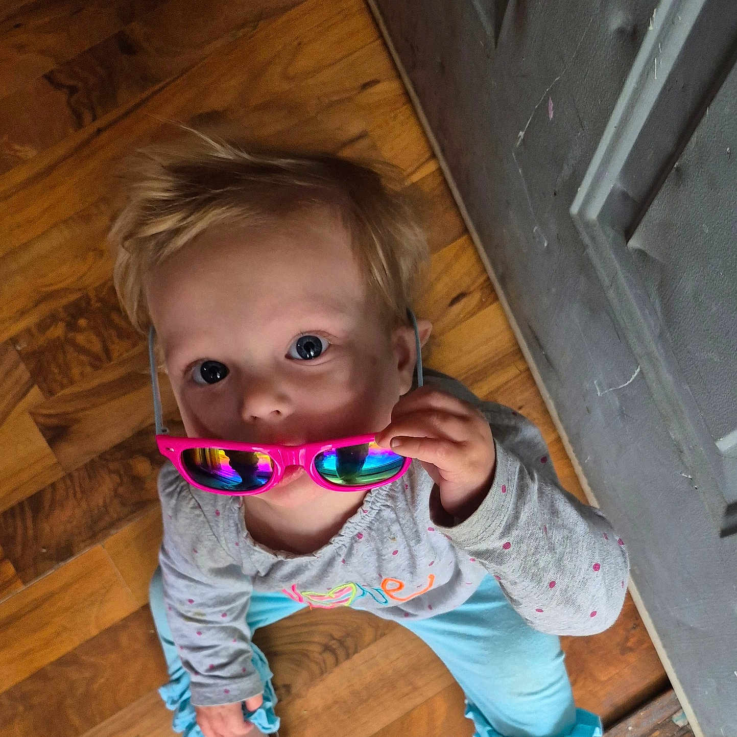 Nova is registered to the contest to win money with this photo: barefoot, blue_pants, casual, child, clothing, curious, floor, gray_door, home, indoor, long_sleeves, looking_up, person, pink, playful, polka_dots, portrait, sunglasses, toddler, wooden_floor
