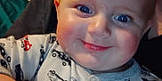Remington is registered to the contest to win money with this photo: baby, child, smiling, blue_eyes, onesie, car_pattern, close_up, face, cheeks, hand, red_hair, infant, cute, happy, indoors, portrait, soft_lighting, cozy, person, young
