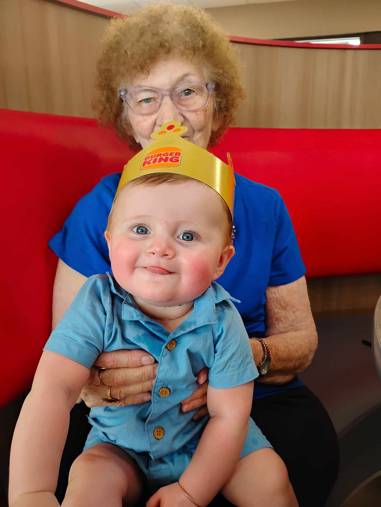 Remington joined the competition — help win amazing prizes! baby, child, elderly_woman, glasses, burger_king_crown, blue_outfit, smile, curly_hair, restaurant, booth, red_cushion, seated, holding, portrait, indoor, happy, person, casual_clothing, skin, hands