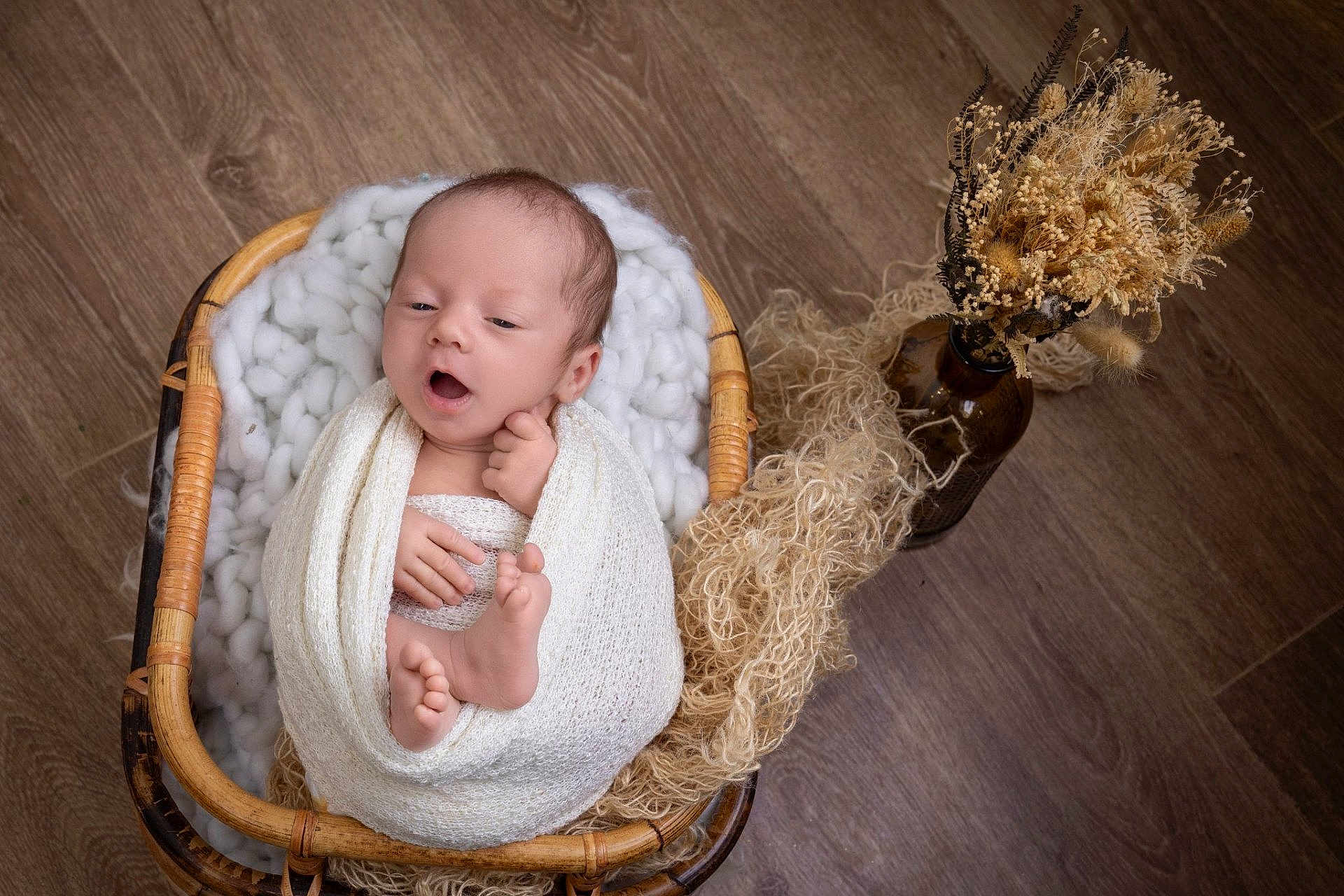 Aaron participe au concours pour gagner de l'argent avec cette photo : baby, newborn, infant, basket, swaddle, blanket, wicker, wood_floor, dried_flowers, vase, props, yawning, toes, hands, cozy, studio, portrait, soft_texture, neutral_tones, natural_decor